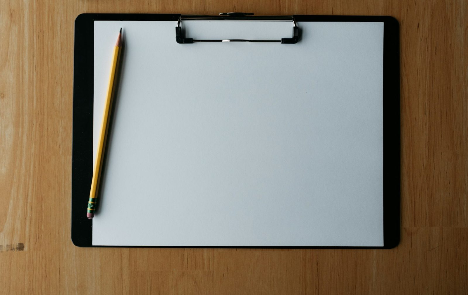 Empty clipboard and a pencil on a wooden desk, seen from above