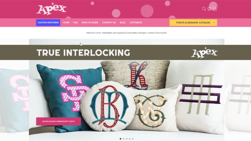 Apex Embroidery Designs storefront with a pink navigation bar and decorative pillows displaying embroidered monograms.